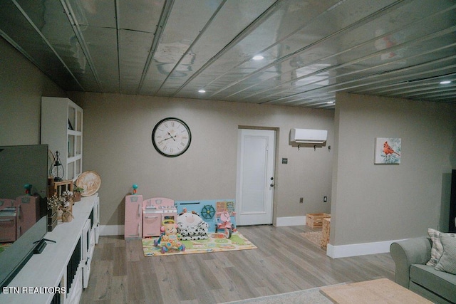 playroom featuring a wall mounted AC, light wood-type flooring, and baseboards