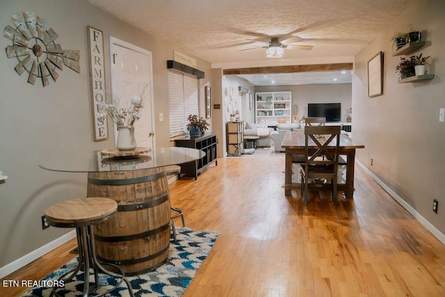 dining area featuring light wood-style floors, beam ceiling, baseboards, and ceiling fan