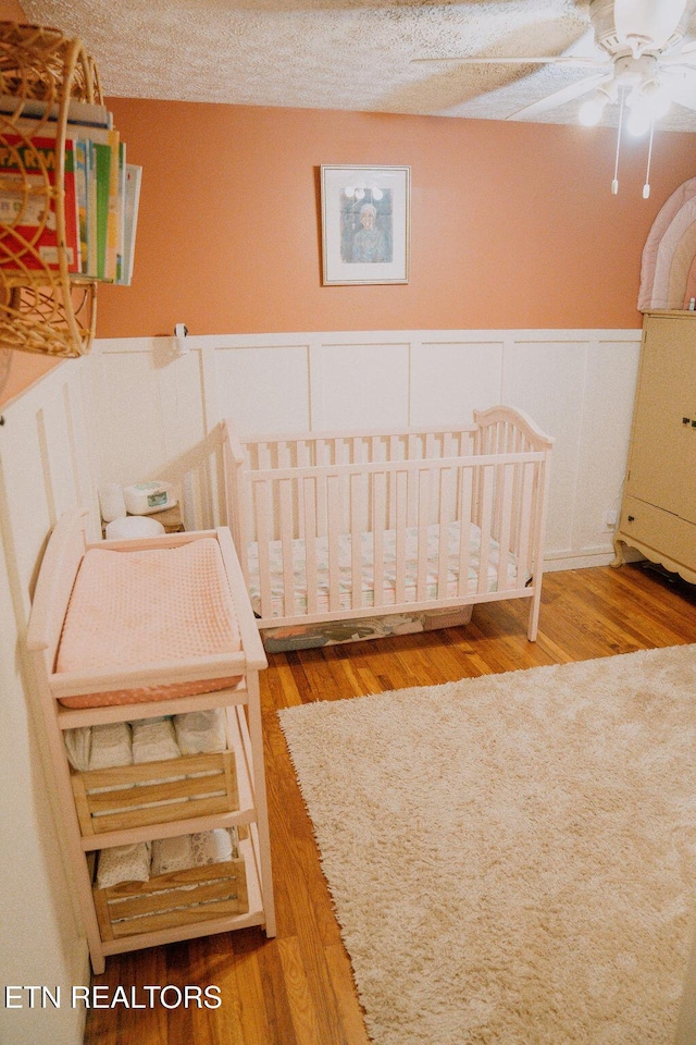 bedroom with wainscoting, wood finished floors, and a decorative wall