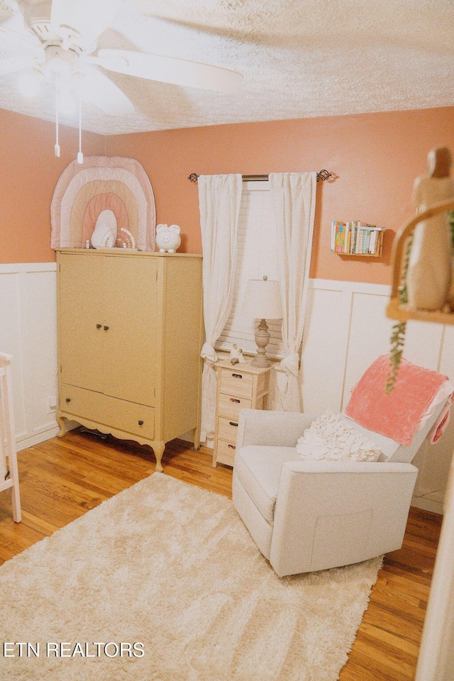 living area featuring light wood-type flooring, a wainscoted wall, a ceiling fan, and a decorative wall