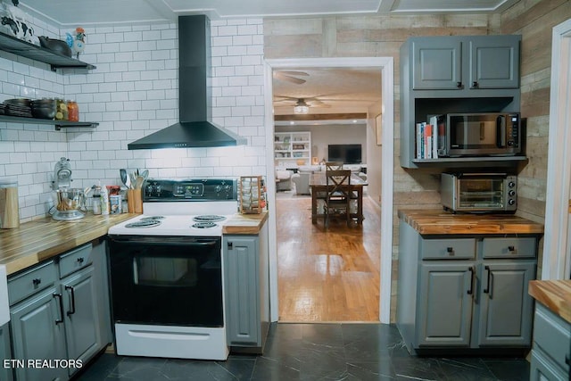 kitchen featuring range with electric cooktop, tasteful backsplash, butcher block countertops, a ceiling fan, and wall chimney range hood