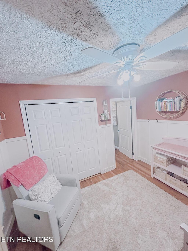 living area with wainscoting, a ceiling fan, wood finished floors, and a textured ceiling