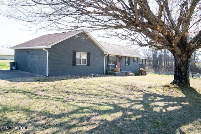 view of side of property featuring brick siding, a lawn, and fence