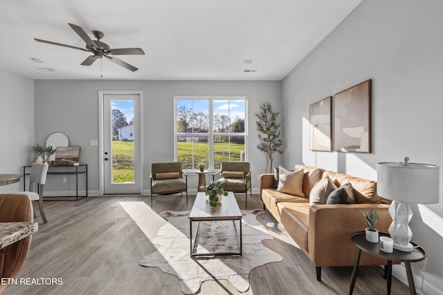 living room featuring wood finished floors, visible vents, baseboards, and ceiling fan
