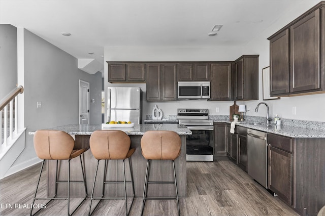kitchen with dark brown cabinets, a kitchen island, appliances with stainless steel finishes, and dark wood-style flooring
