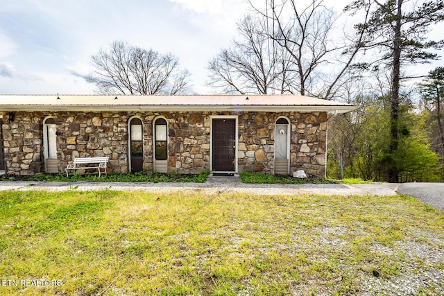 view of front of house featuring a front yard, metal roof, and stone siding