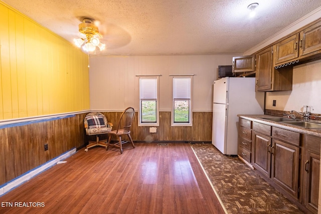 kitchen with a sink, a textured ceiling, wood walls, a ceiling fan, and dark wood-style floors