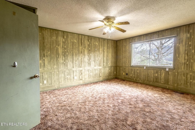 spare room with wooden walls, a ceiling fan, carpet flooring, and a textured ceiling