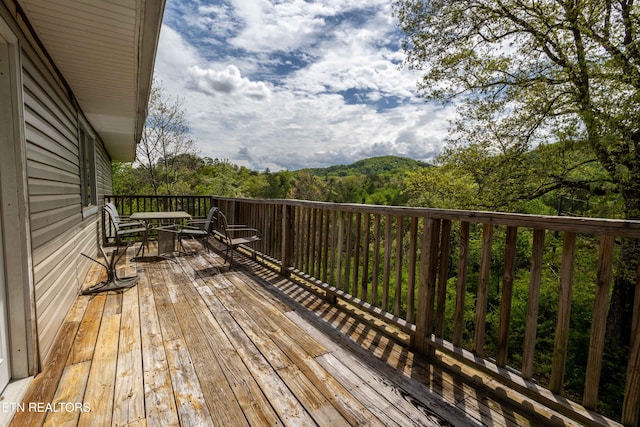 wooden deck featuring outdoor dining area and a view of trees