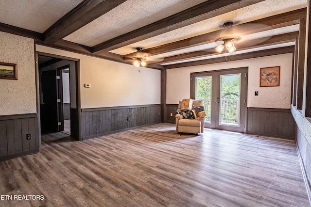 sitting room featuring wood finished floors, ceiling fan, a wainscoted wall, and beamed ceiling