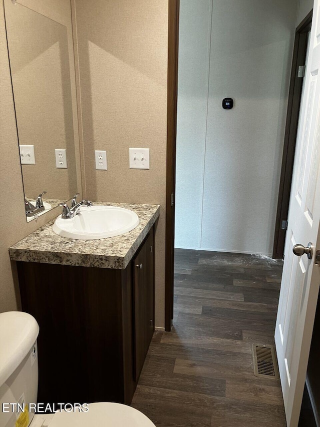 half bath featuring visible vents, toilet, vanity, and wood finished floors