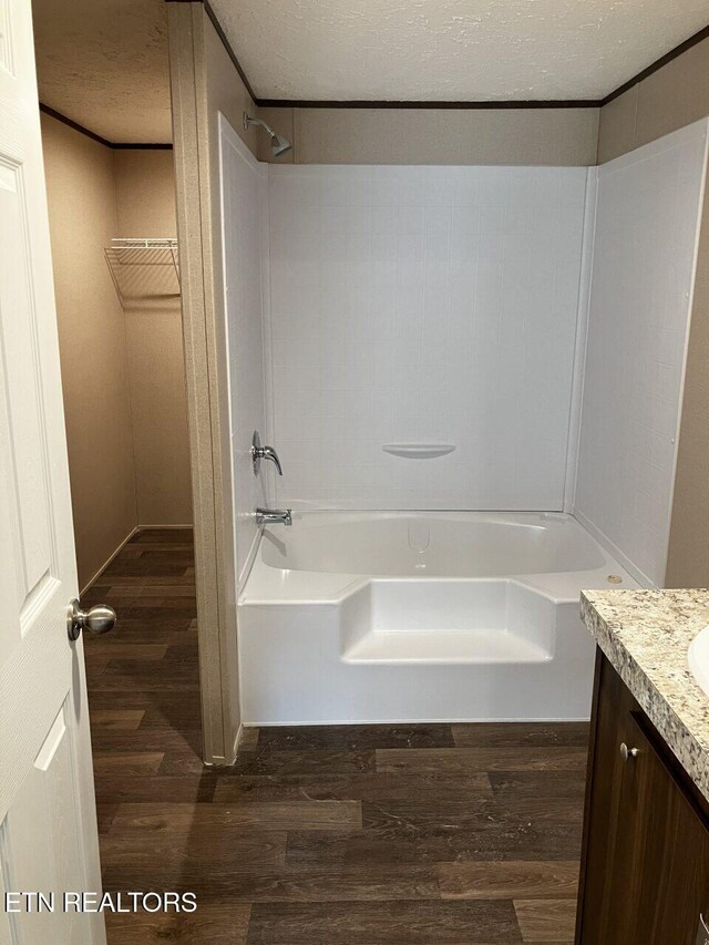 full bath featuring a textured ceiling, wood finished floors, vanity, bathing tub / shower combination, and a spacious closet