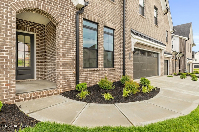 entrance to property featuring concrete driveway, an attached garage, and brick siding