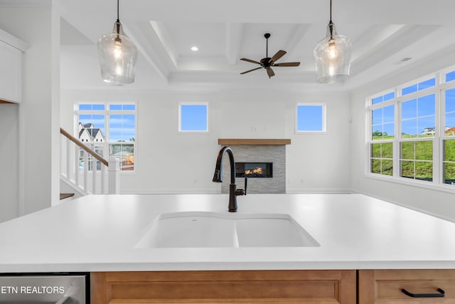 kitchen featuring a sink, ceiling fan, light countertops, and a glass covered fireplace