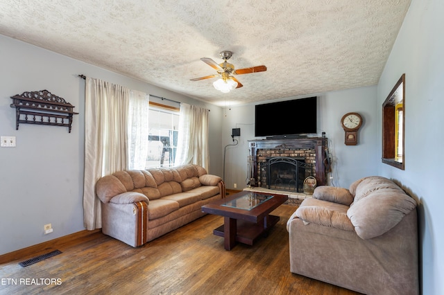 living area with a ceiling fan, wood finished floors, a brick fireplace, baseboards, and visible vents