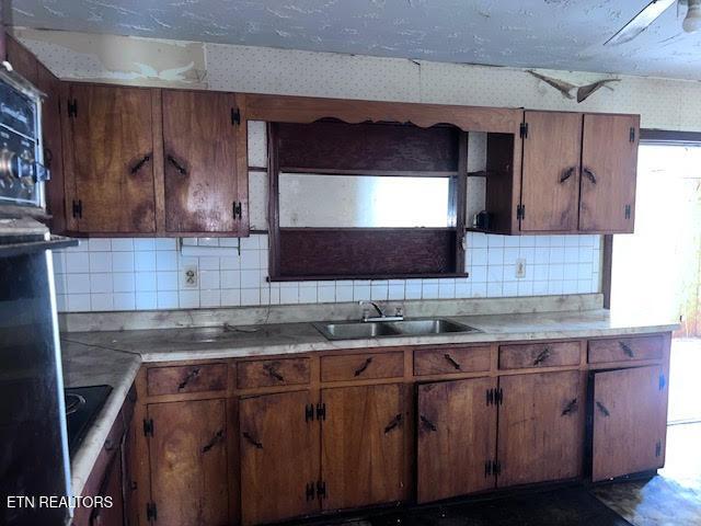 kitchen with light countertops, brown cabinetry, a sink, and tasteful backsplash