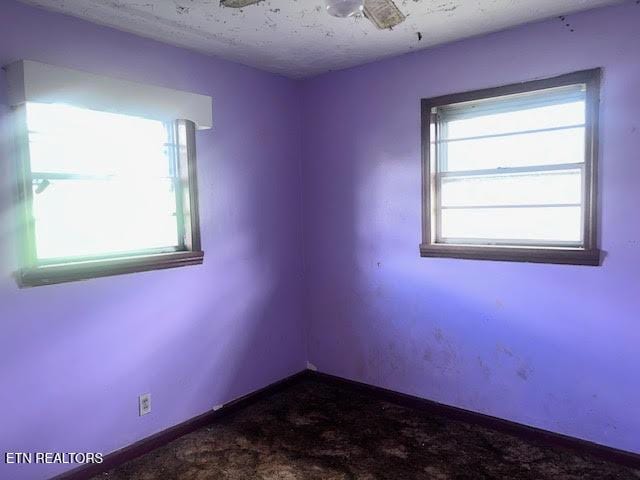 unfurnished room with dark colored carpet, plenty of natural light, baseboards, and a textured ceiling