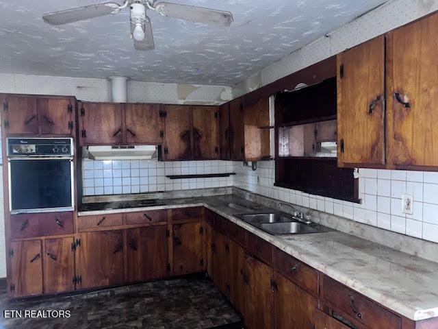 kitchen with under cabinet range hood, a sink, black appliances, and decorative backsplash