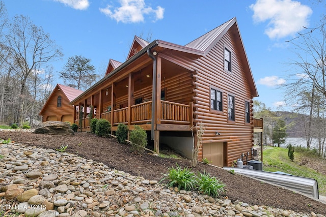 view of side of home with covered porch, cooling unit, an attached garage, log exterior, and metal roof