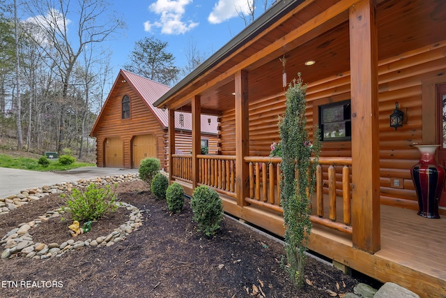 view of side of property with an outbuilding, concrete driveway, metal roof, log exterior, and a porch