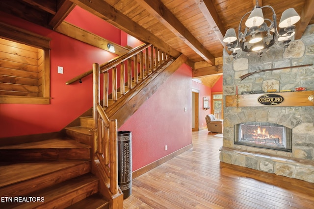 staircase with a notable chandelier, wood-type flooring, baseboards, wood ceiling, and a stone fireplace