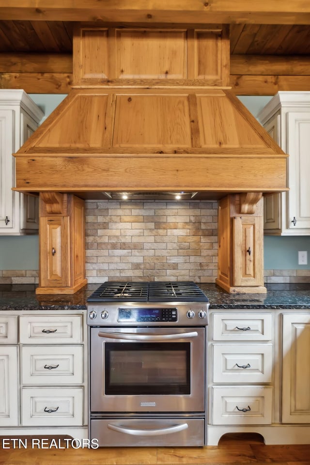 kitchen featuring dark stone counters, stainless steel range with gas stovetop, decorative backsplash, and white cabinets