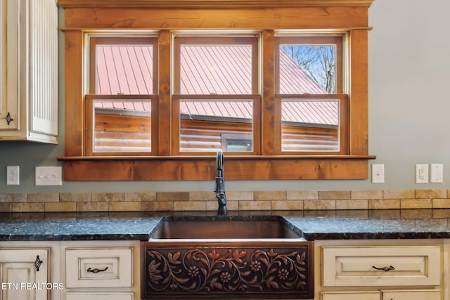 interior space with cream cabinetry, a sink, and dark stone countertops
