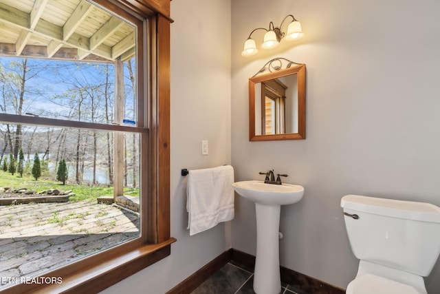 half bath featuring baseboards, toilet, tile patterned flooring, and a sink