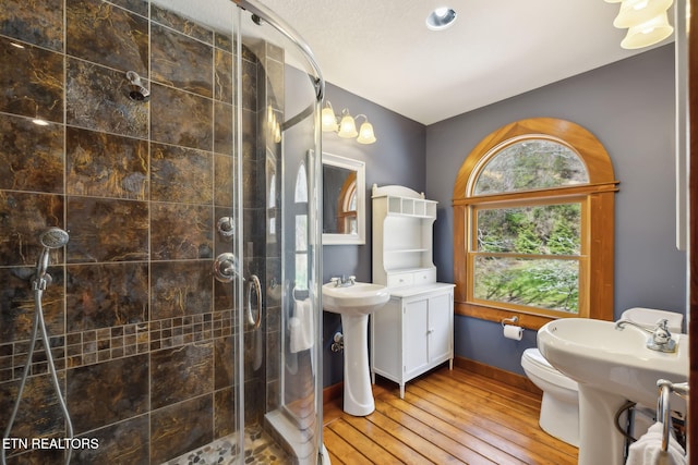 bathroom with baseboards, wood finished floors, toilet, and a shower stall