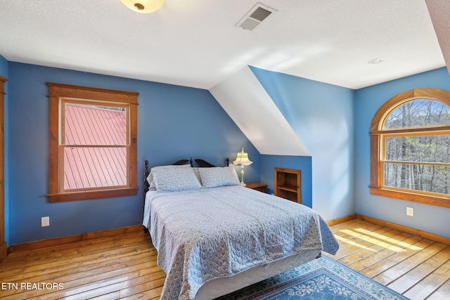 bedroom with baseboards, visible vents, lofted ceiling, and wood-type flooring