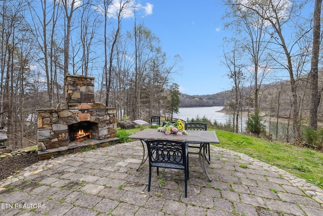 view of patio featuring a water view, outdoor dining area, and an outdoor stone fireplace