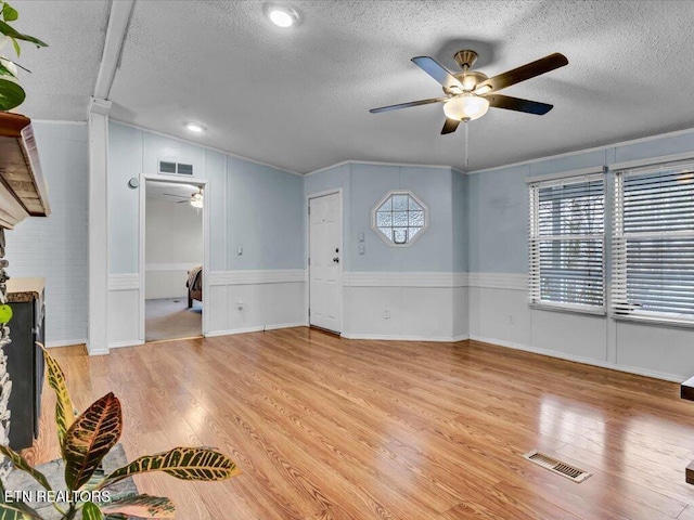 unfurnished living room featuring light wood-type flooring, visible vents, a textured ceiling, and a ceiling fan