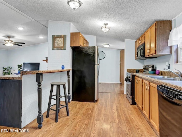 kitchen with a textured ceiling, black appliances, light wood-style floors, ceiling fan, and a sink