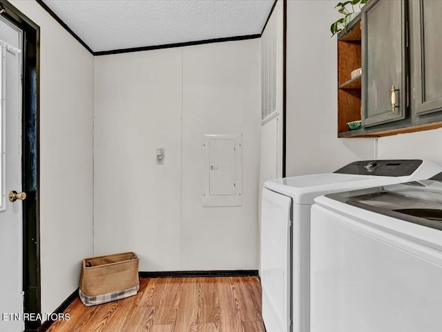 laundry area with a textured ceiling, electric panel, washing machine and clothes dryer, light wood finished floors, and cabinet space