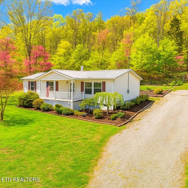 ranch-style house with a standing seam roof, covered porch, metal roof, a front yard, and driveway