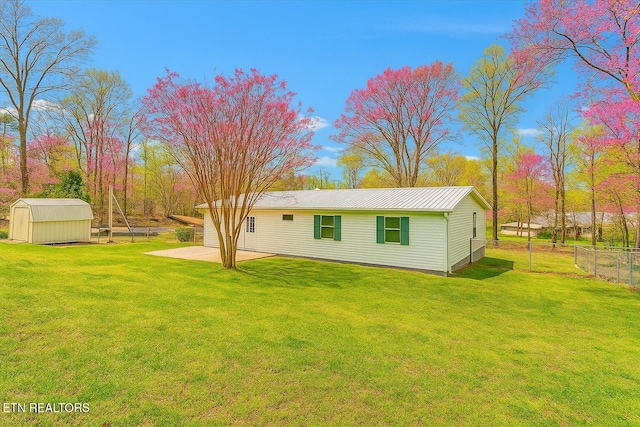 rear view of property featuring an outbuilding, a shed, a lawn, a patio, and metal roof