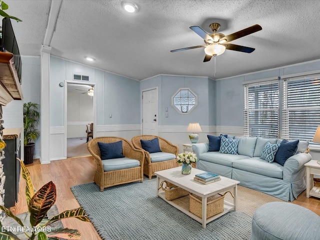 living room featuring a wainscoted wall, wood finished floors, visible vents, a textured ceiling, and ceiling fan