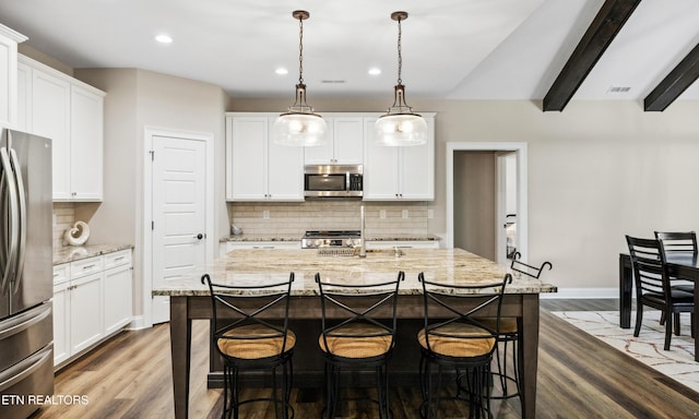 kitchen featuring stainless steel appliances, tasteful backsplash, a kitchen breakfast bar, white cabinets, and a center island with sink
