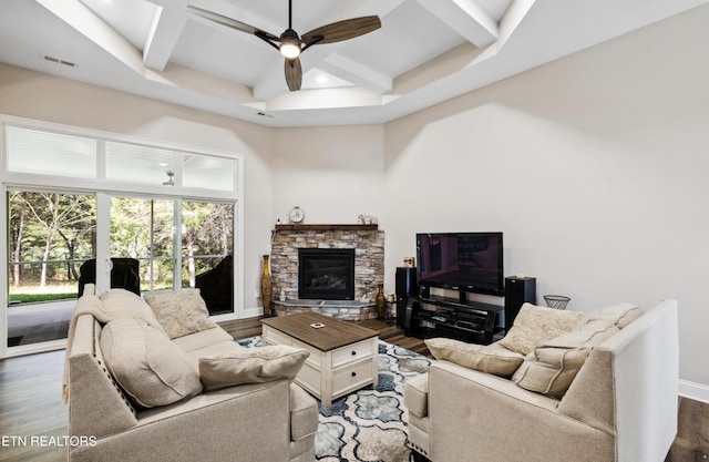 living room featuring wood finished floors, coffered ceiling, a ceiling fan, beam ceiling, and a stone fireplace