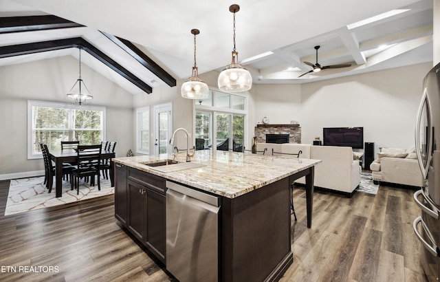 kitchen with a sink, appliances with stainless steel finishes, a stone fireplace, dark wood-style flooring, and a ceiling fan