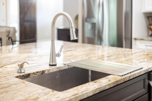 kitchen view of a sink, light stone countertops, and stainless steel fridge