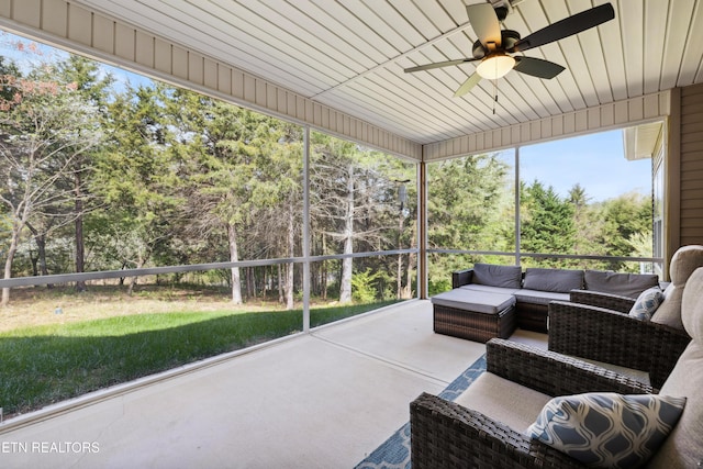 sunroom / solarium featuring a ceiling fan, an outdoor living space, and view of wooded area