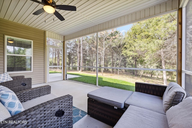 sunroom / solarium featuring ceiling fan and view of scattered trees