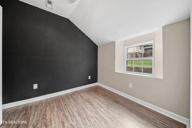 unfurnished room with baseboards, lofted ceiling, visible vents, and wood finished floors