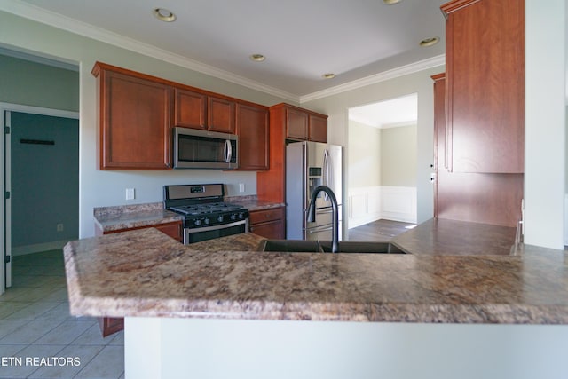 kitchen with a wainscoted wall, tile patterned floors, crown molding, a sink, and appliances with stainless steel finishes