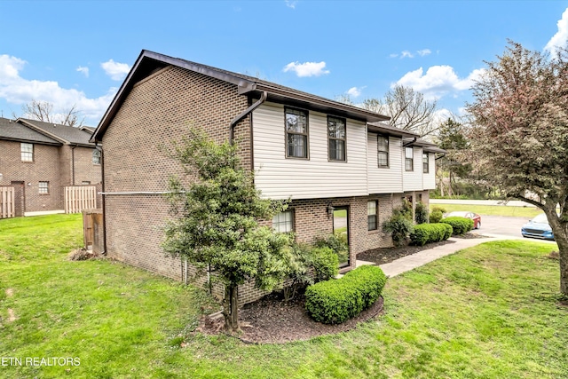 view of side of home with brick siding, fence, and a yard