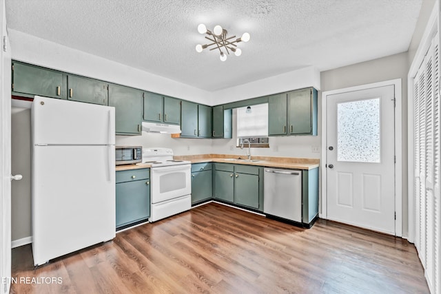 kitchen with green cabinets, under cabinet range hood, a sink, stainless steel appliances, and a notable chandelier