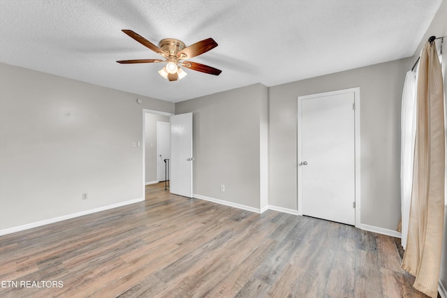 unfurnished bedroom with a textured ceiling, wood finished floors, baseboards, and a ceiling fan