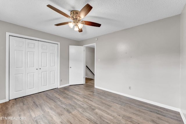 unfurnished bedroom with a closet, baseboards, wood finished floors, and a textured ceiling