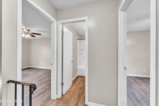 hallway with baseboards, wood finished floors, and a textured ceiling